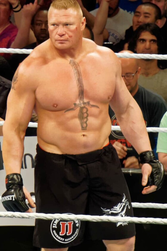 WWE and MMA star Brock Lesnar standing in a ring. He is a muscular giant with a sword tattoo in the middle of his chest.