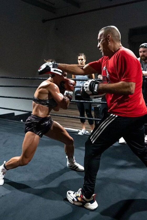 Fitness bodybuilder Stefi Cohen sparring with her coach to train for her next fight. She is dodging a strike with her muscles fully flexed and engaged.
