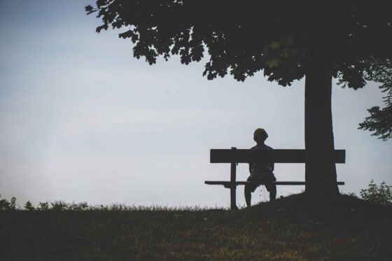 Boy sitting under a tree on a bench by himself