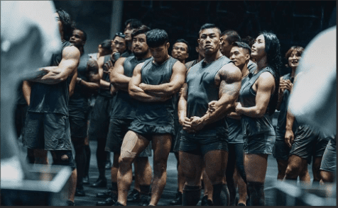 Physical 100 competitors standing around waiting for their next challenge in grey excercise outfits.