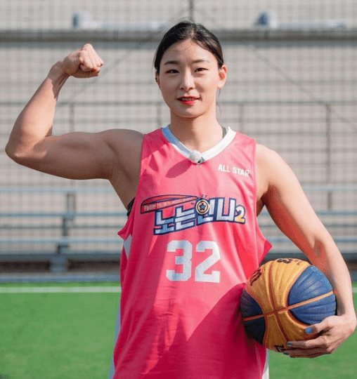 Wrestler Jang Eun Sil flexing a large bicep while holding a basketball. She is wearing a pink jersey with the number 32.