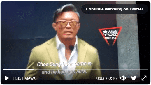 Choo Sung-Hoon sporting yellow glasses, coiffed hair, and a stylish suit jacket.